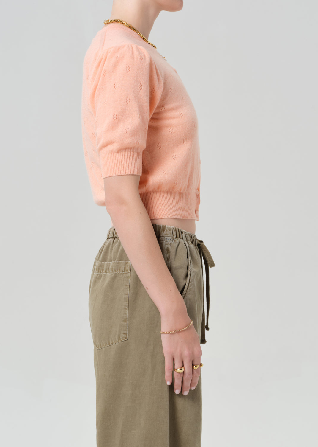 Person wearing a peach cardigan and brown pants on a gray background