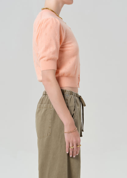 Person wearing a peach cardigan and brown pants on a gray background