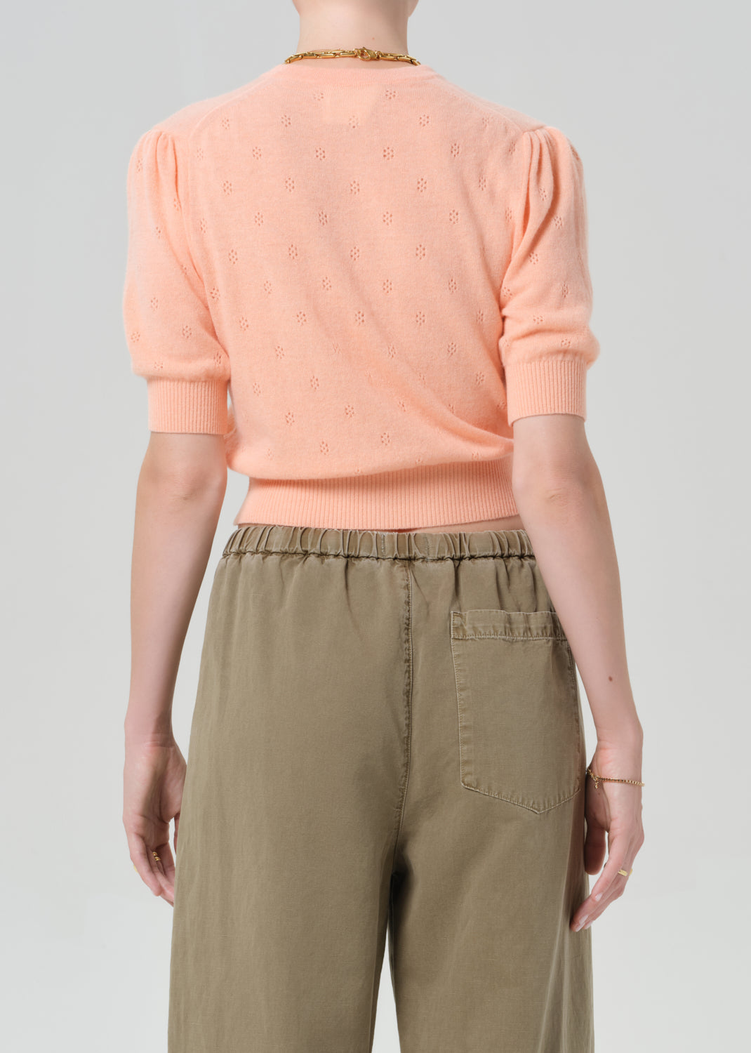 Person wearing a peach cardigan and brown pants on a gray background
