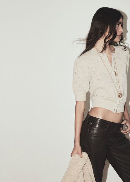 Person wearing a beige cardigan and brown leather pants on a plain background