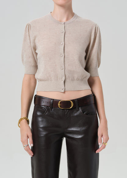 Person wearing a beige cardigan and brown leather pants on a plain background