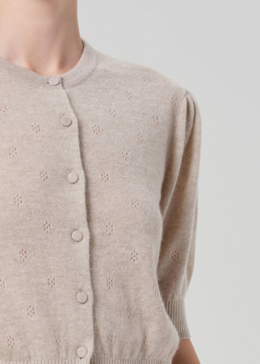 Person wearing a beige cardigan and brown leather pants on a plain background