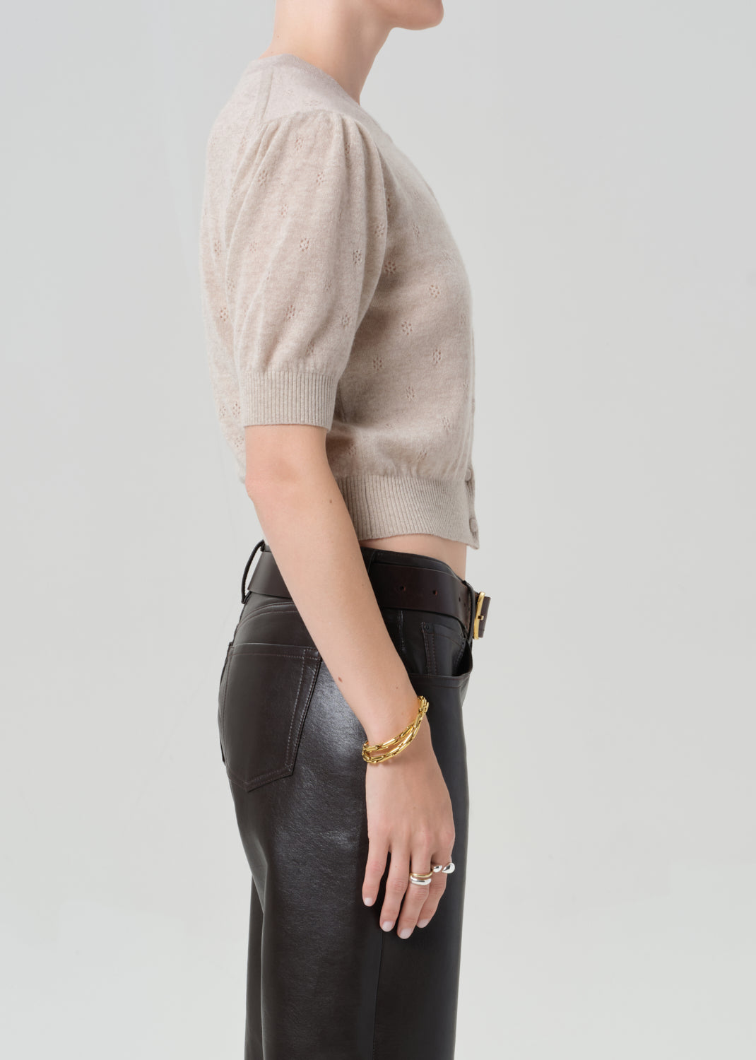Person wearing a beige cardigan and brown leather pants on a plain background
