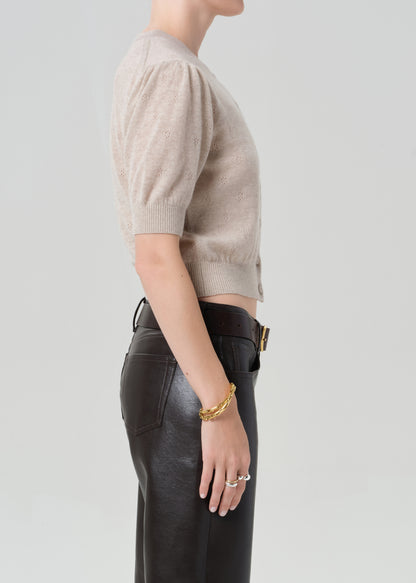 Person wearing a beige cardigan and brown leather pants on a plain background