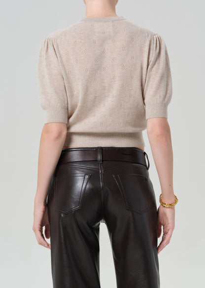 Person wearing a beige cardigan and brown leather pants on a plain background