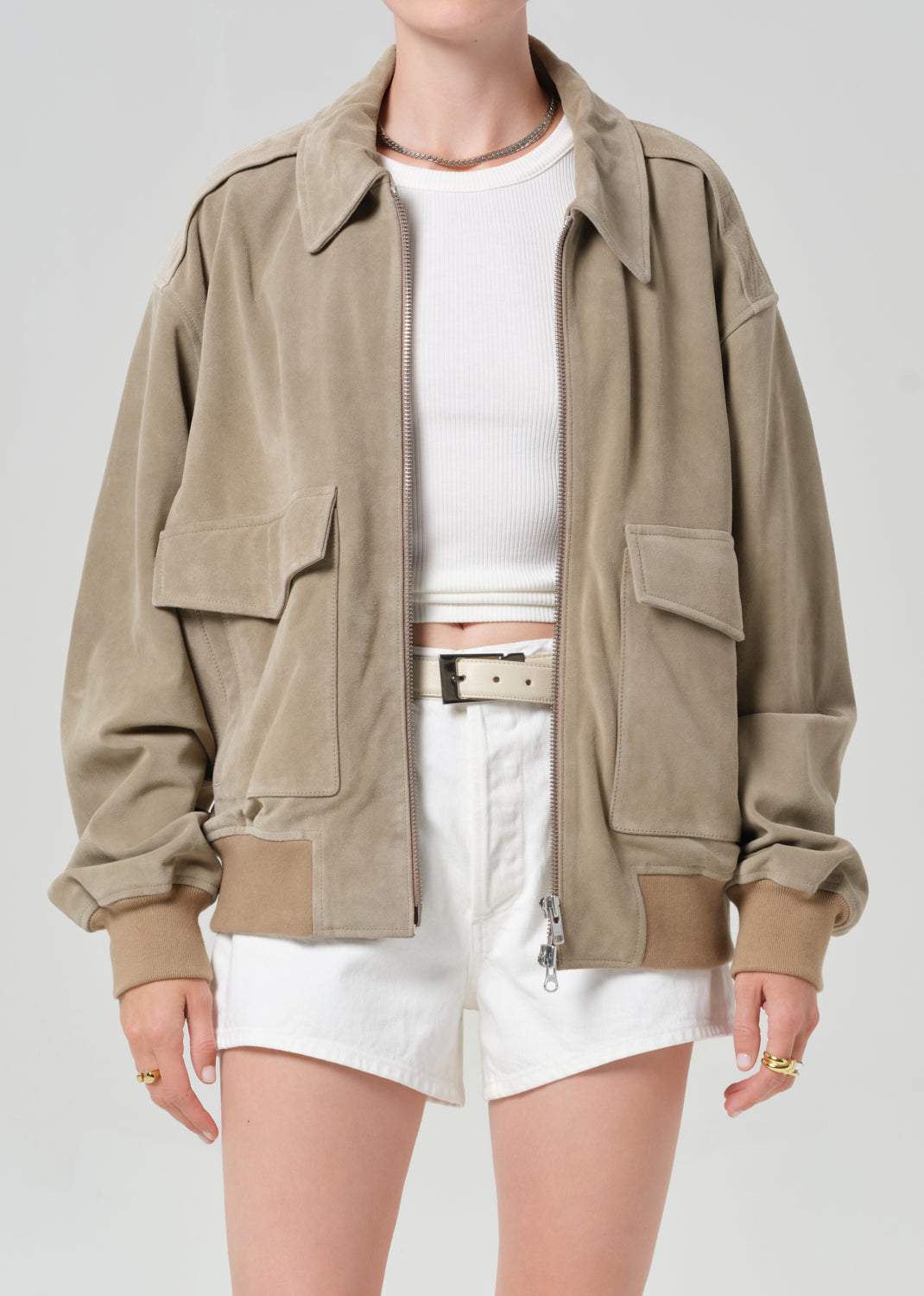 Person wearing a suede jacket over a white shirt and shorts on a light gray background