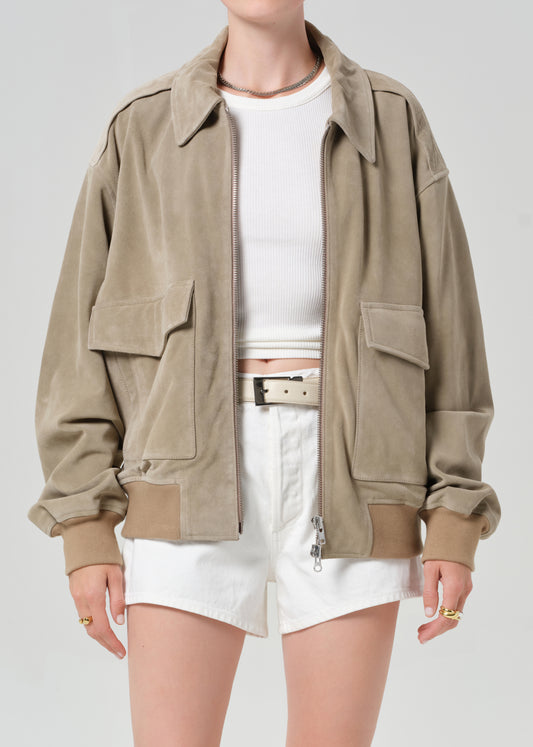 Person wearing a suede jacket over a white shirt and shorts on a light gray background