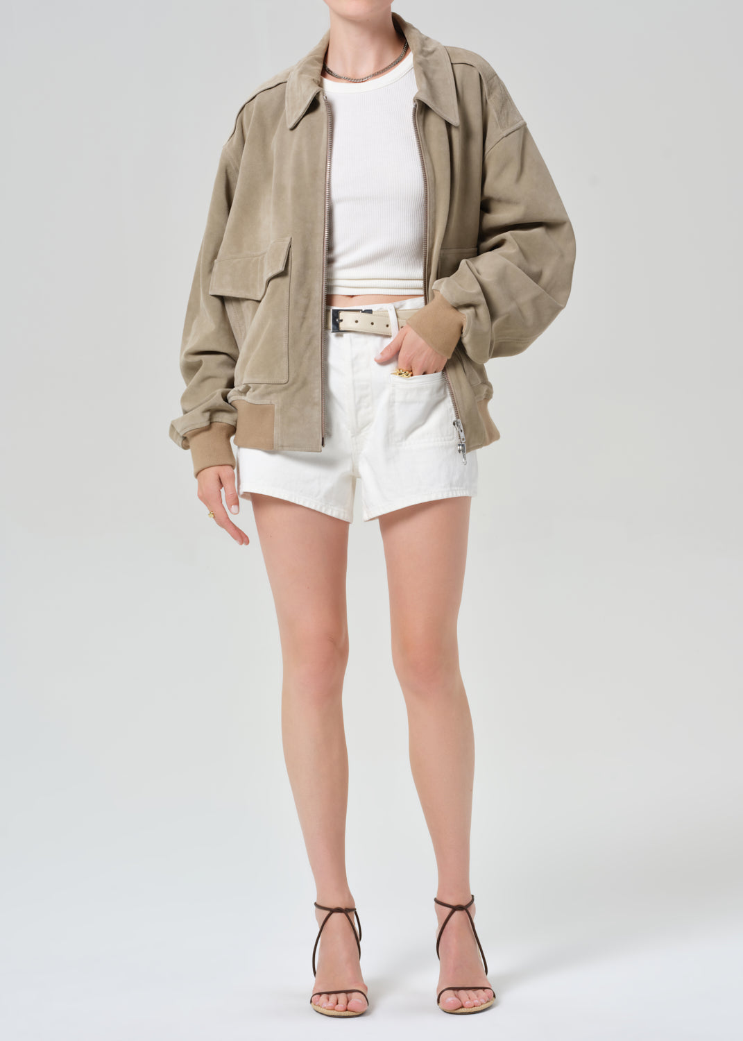 Person wearing a suede jacket over a white shirt and shorts on a light gray background