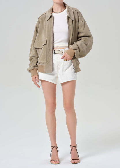 Person wearing a suede jacket over a white shirt and shorts on a light gray background