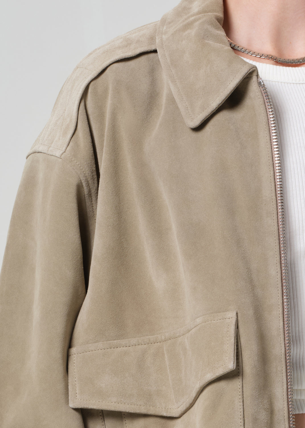 Person wearing a suede jacket over a white shirt and shorts on a light gray background