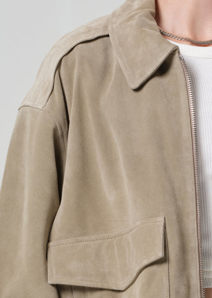 Person wearing a suede jacket over a white shirt and shorts on a light gray background