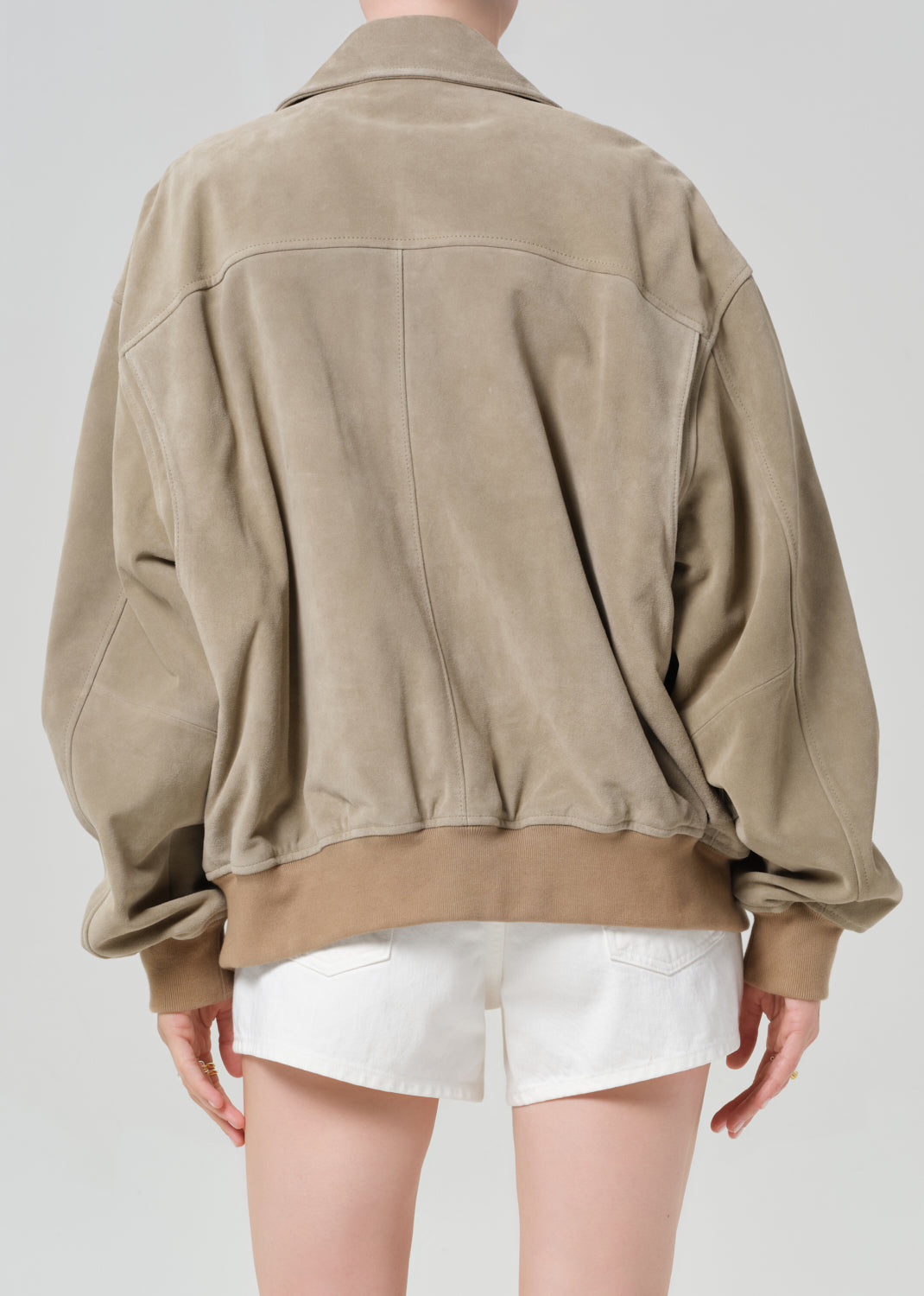 Person wearing a suede jacket over a white shirt and shorts on a light gray background