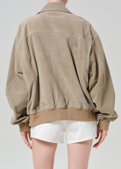 Person wearing a suede jacket over a white shirt and shorts on a light gray background