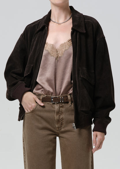 A model wearing an oversized dark brown corduroy jacket over a mauve satin camisole with lace trim, paired with brown jeans and a brown belt, against a solid grey background.
