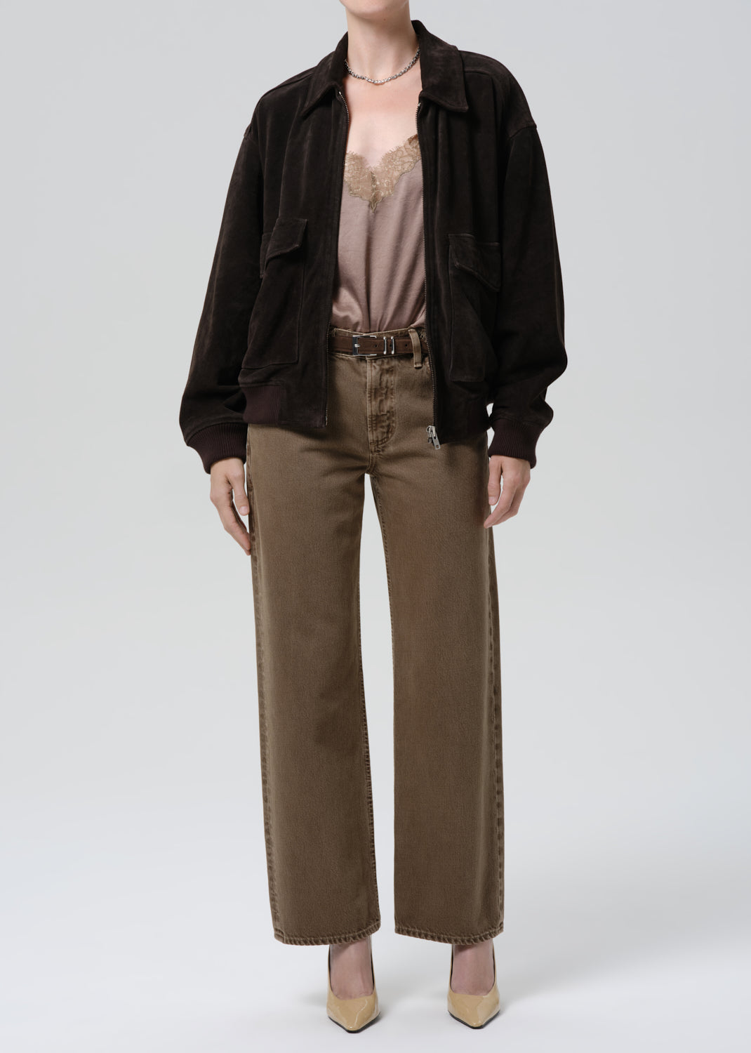 Person wearing a dark brown shirt, beige top, and brown pants on a grey background