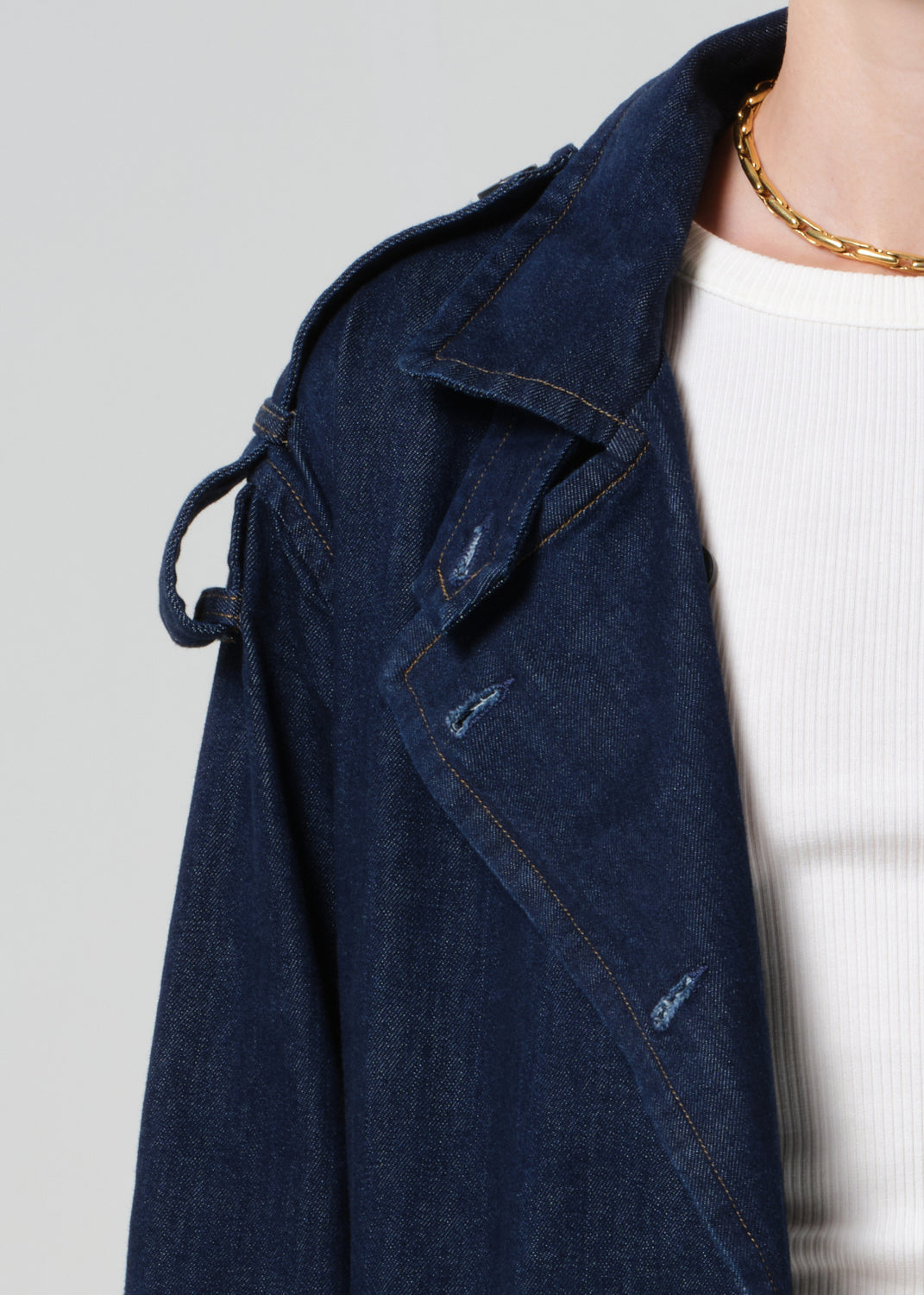 Person wearing long denim trench coat in dark indigo paired with jeans