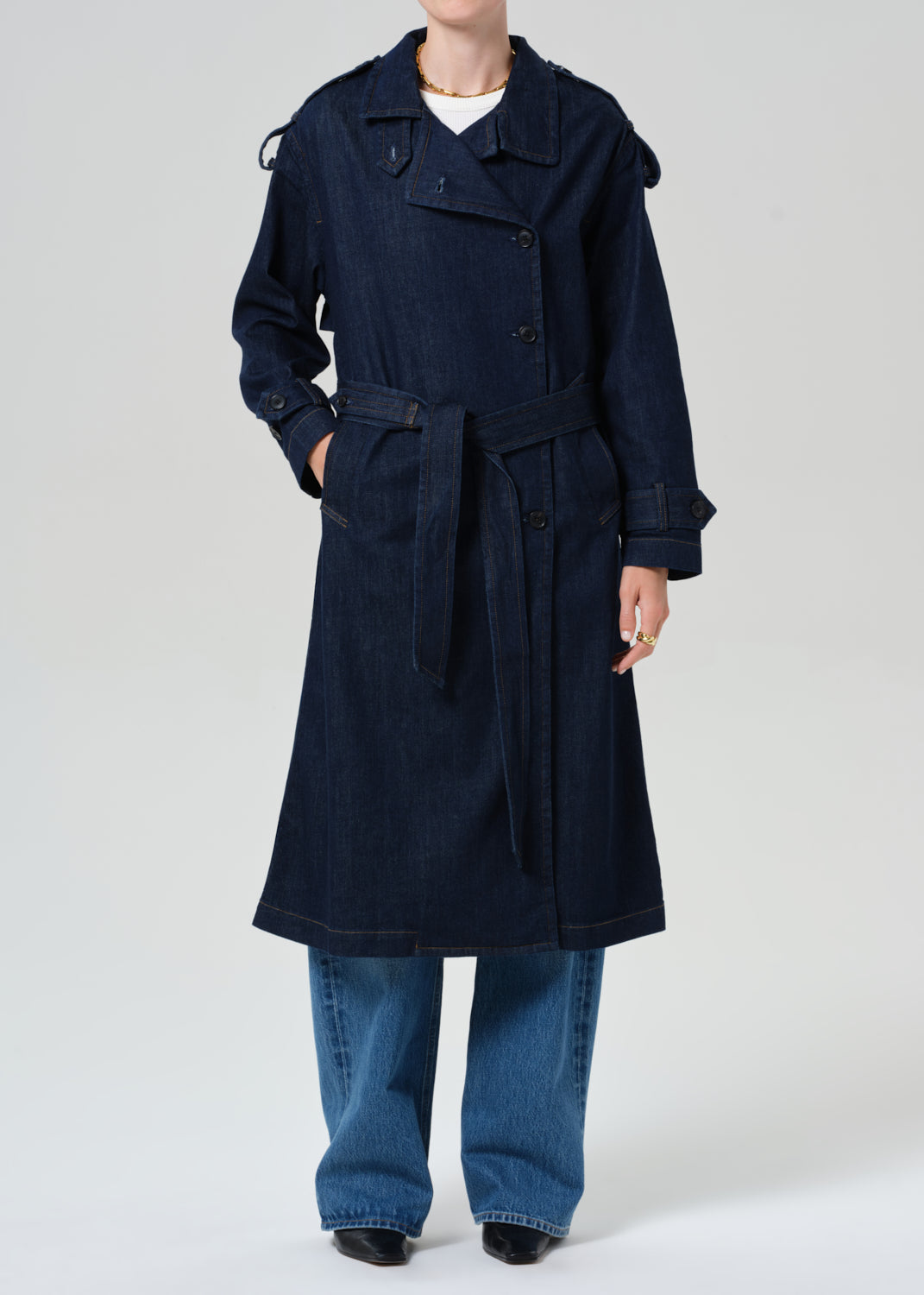 Person wearing long denim trench coat in dark indigo paired with jeans