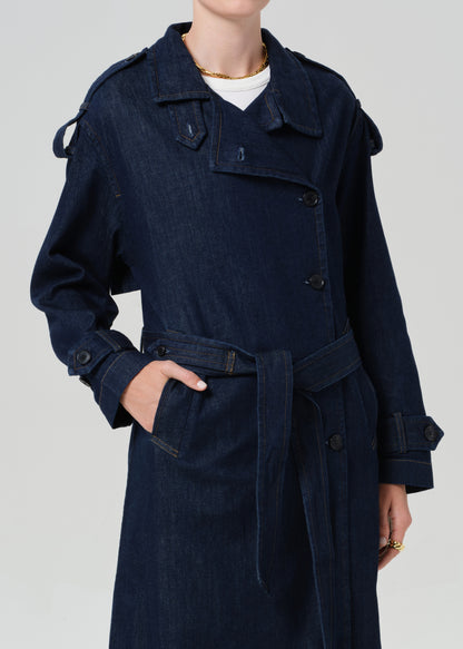 Person wearing long denim trench coat in dark indigo paired with jeans