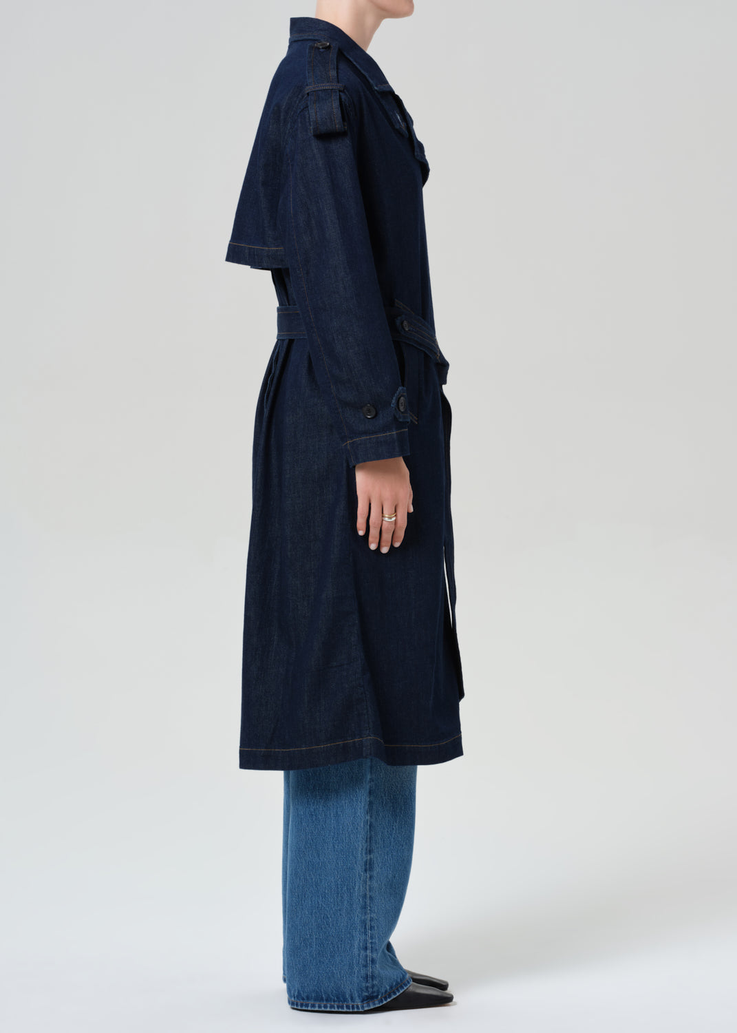 Person wearing long denim trench coat in dark indigo paired with jeans