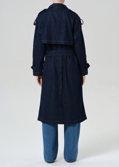 Person wearing long denim trench coat in dark indigo paired with jeans