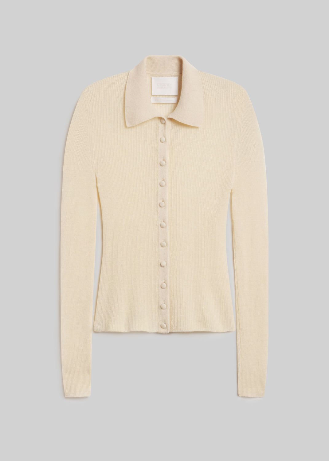 Paloma Cardigan Sweater in Cream, featuring a fitted silhouette, fine ribbed knit, pointed collar, long sleeves, and tonal buttons down the front, front view on a grey background.