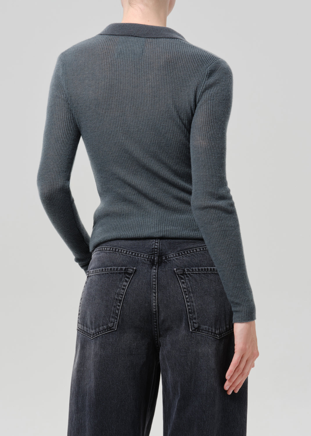 Person wearing a charcoal ribbed collared cardigan with black wide leg jeans viewed from the back on a grey background