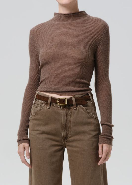 Person wearing a brown ribbed sweater and matching pants on a grey background