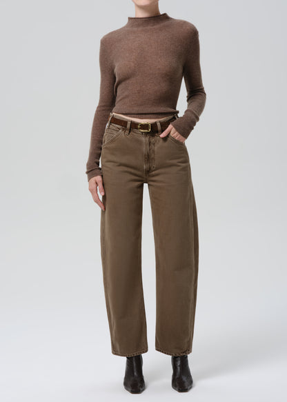 Person wearing a brown turtleneck and wide-leg pants on a grey background