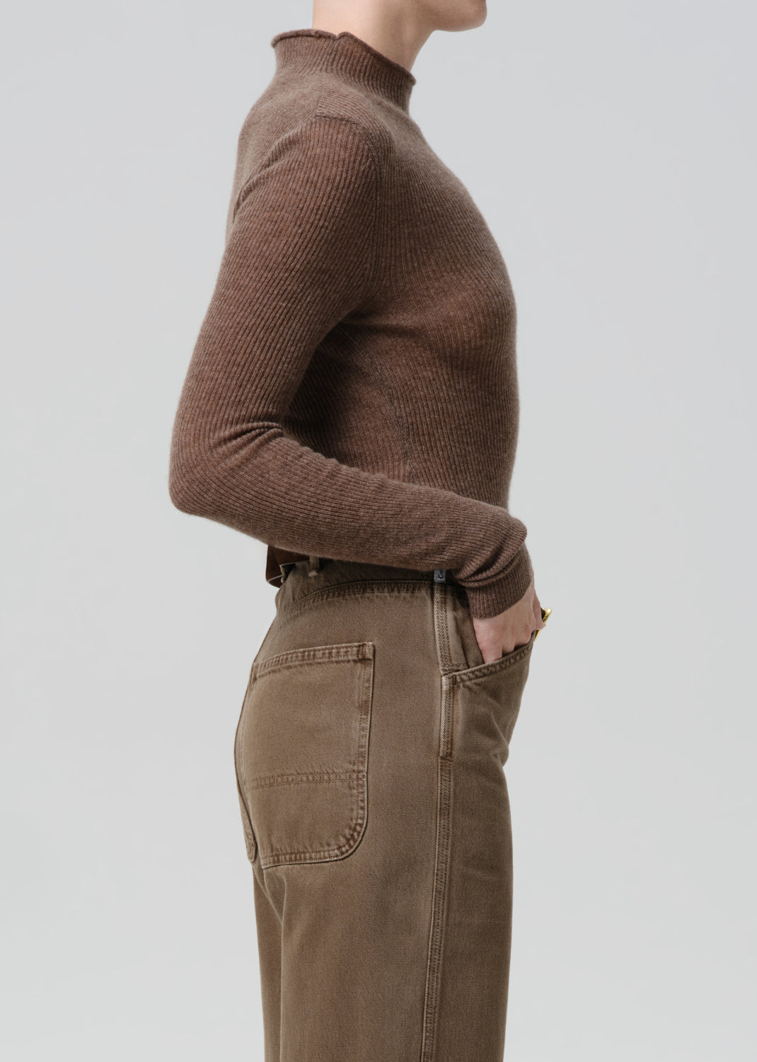 Person wearing a brown ribbed sweater and brown pants on a grey background