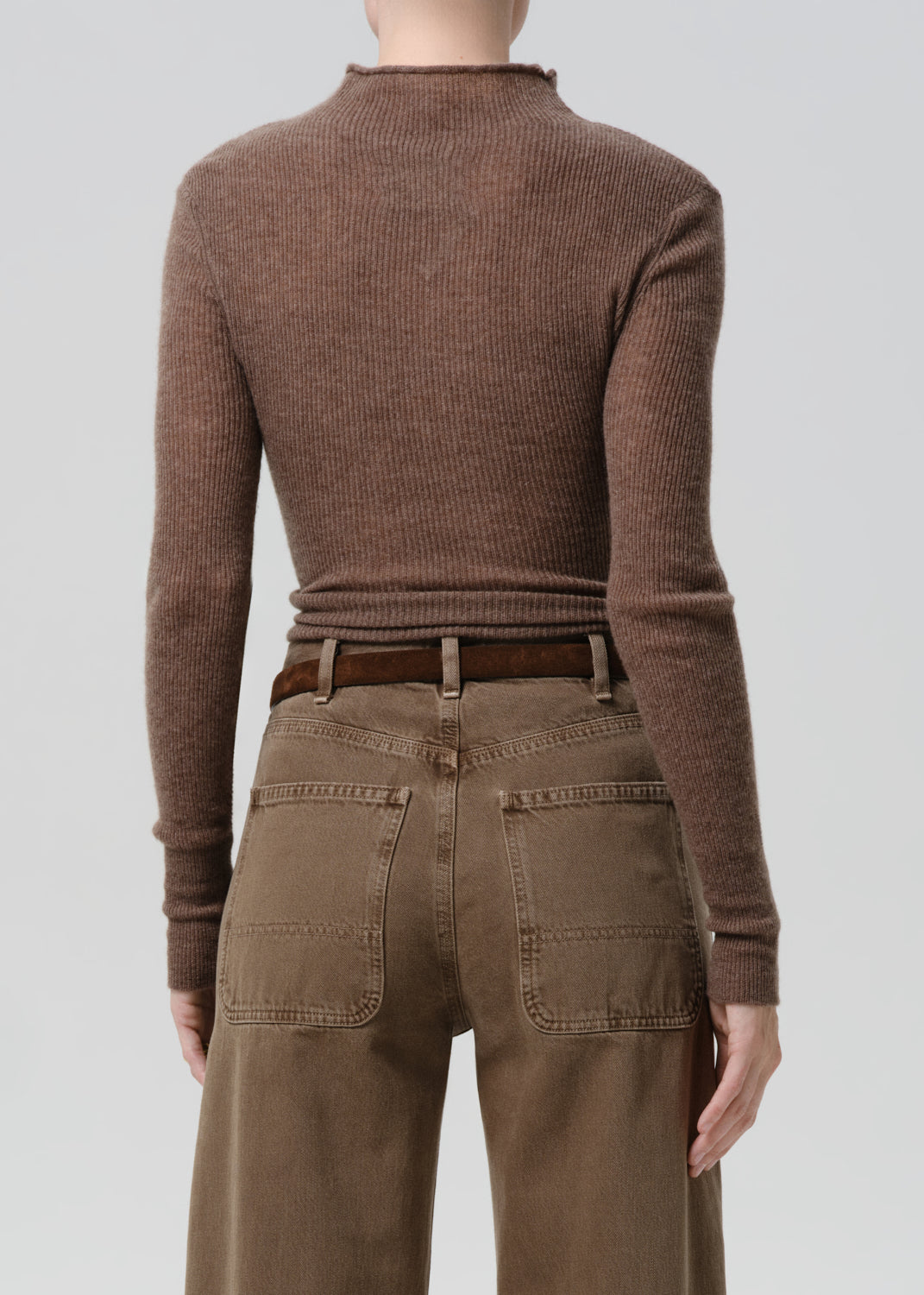 Person wearing a brown ribbed sweater and brown pants on a grey background