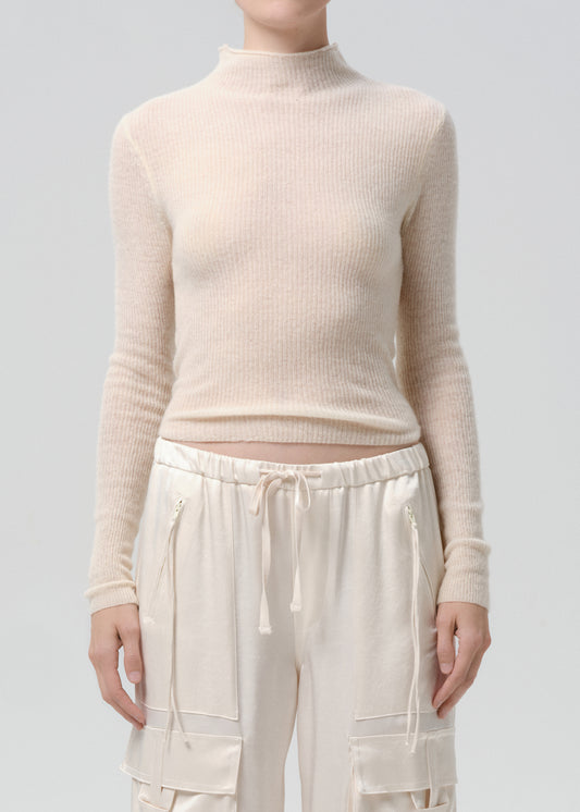 Person wearing a beige ribbed sweater and cream pants on a grey background