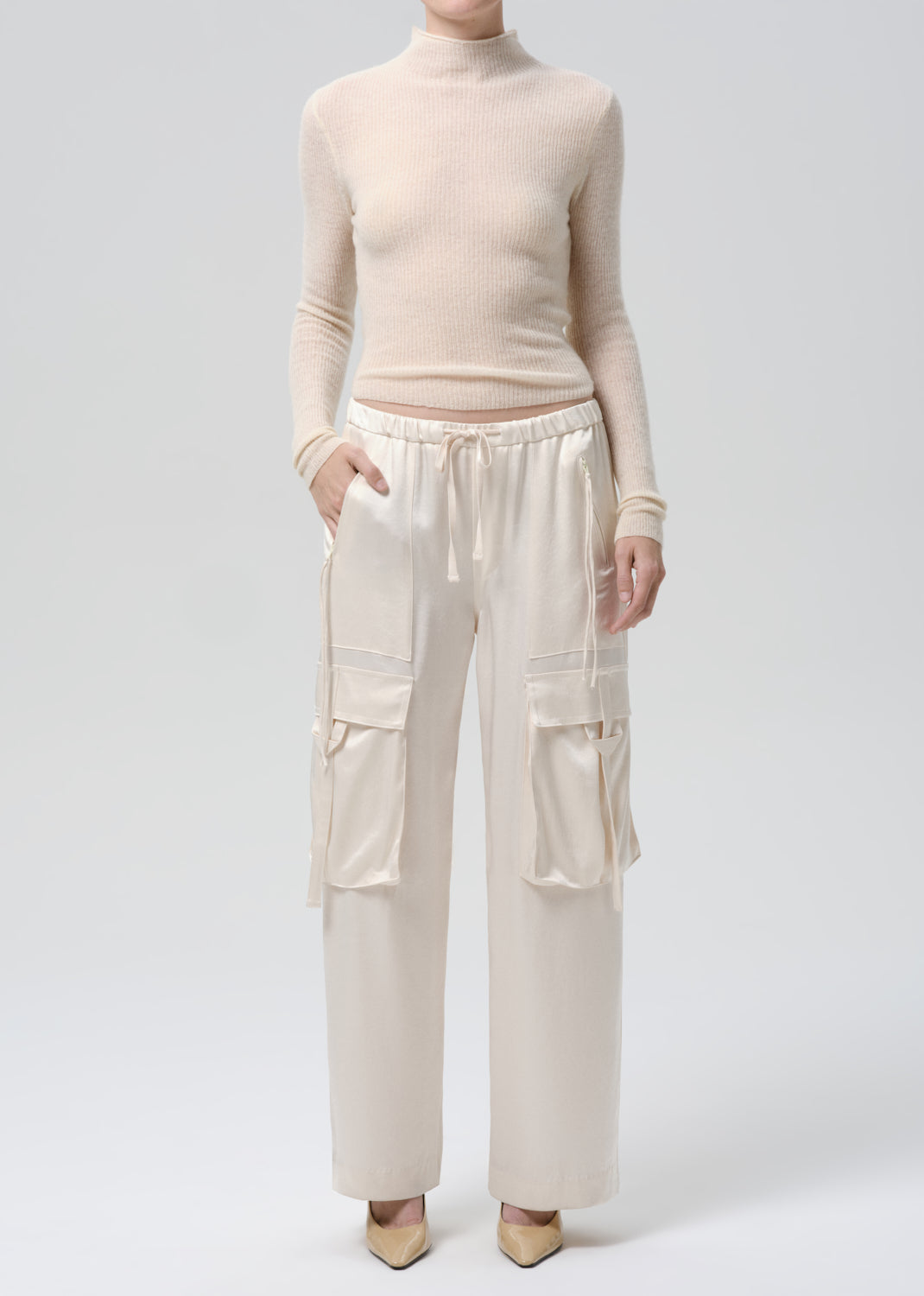 Person wearing a beige turtleneck and cargo pants on a grey background