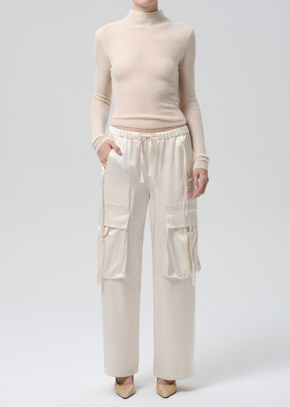 Person wearing a beige turtleneck and cargo pants on a grey background
