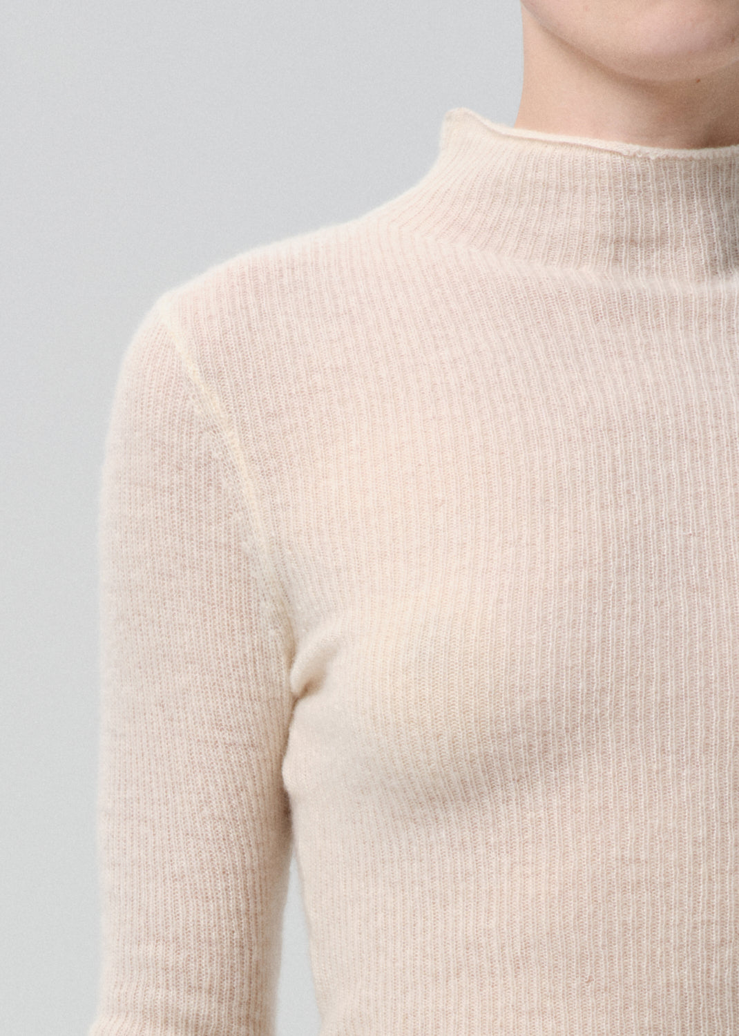 Close-up of a person wearing a beige ribbed sweater against a grey background