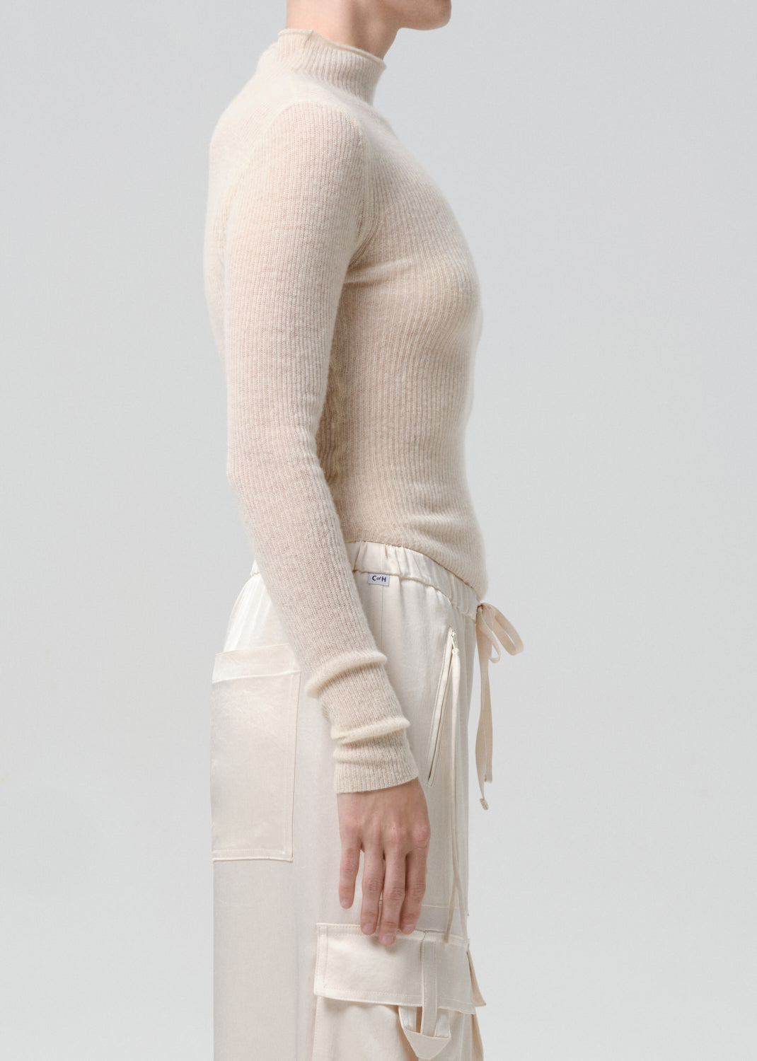 Person wearing a cream long-sleeve top and white pants on a grey background
