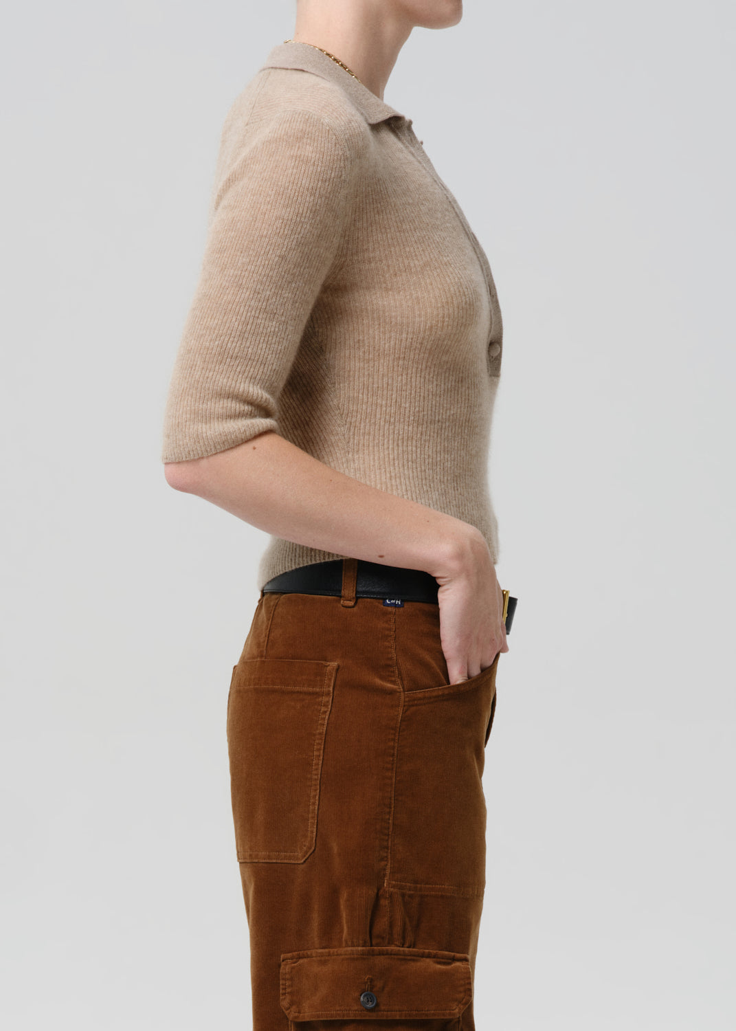 Person wearing a beige short-sleeve shirt and brown pants on a grey background