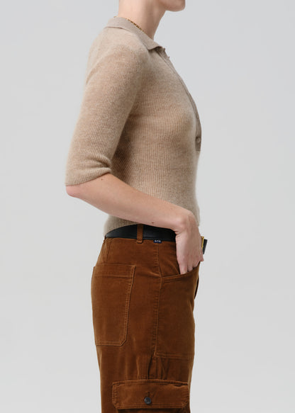 Person wearing a beige short-sleeve shirt and brown pants on a grey background