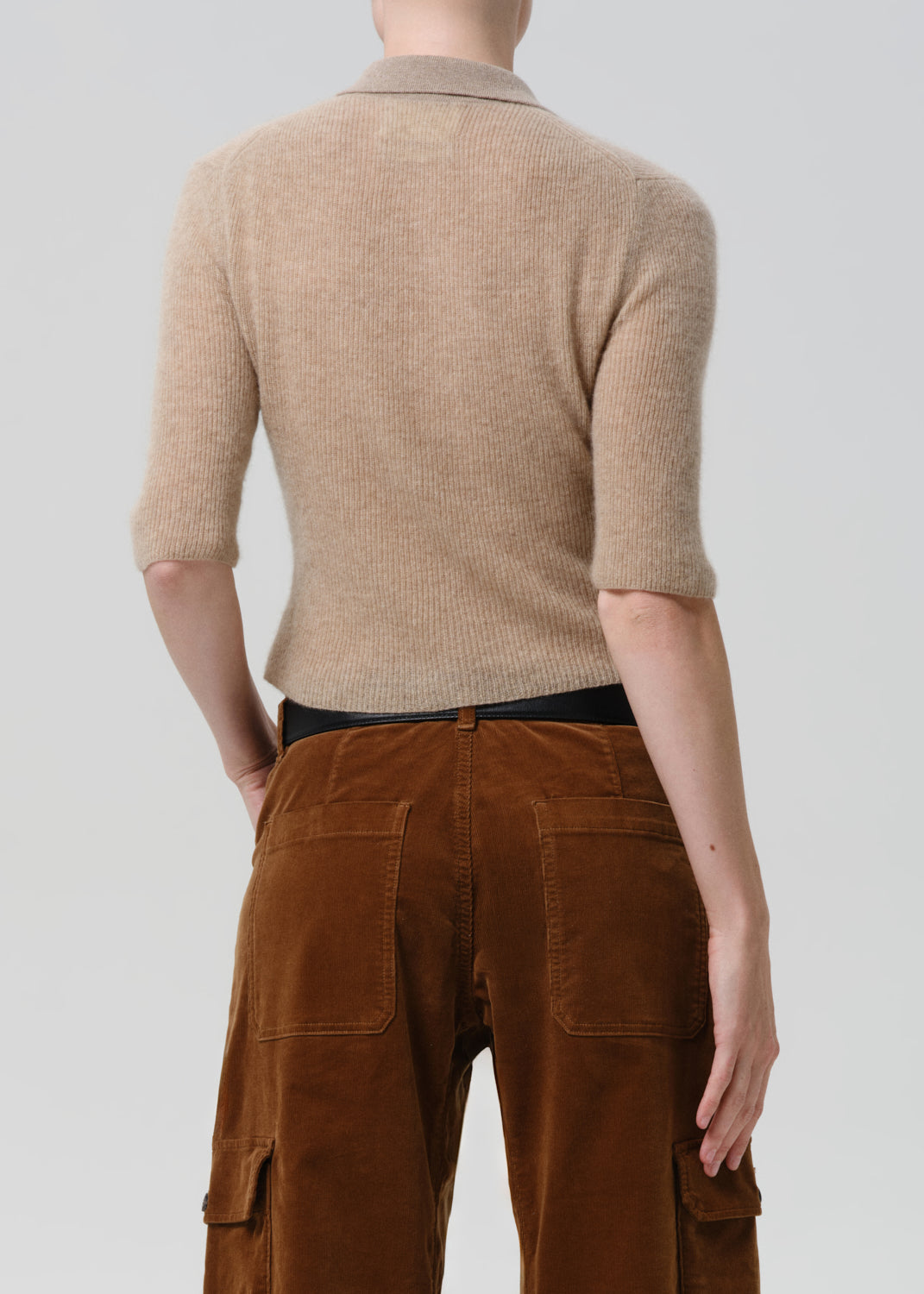 Person wearing a beige ribbed sweater and brown cargo pants on a grey background