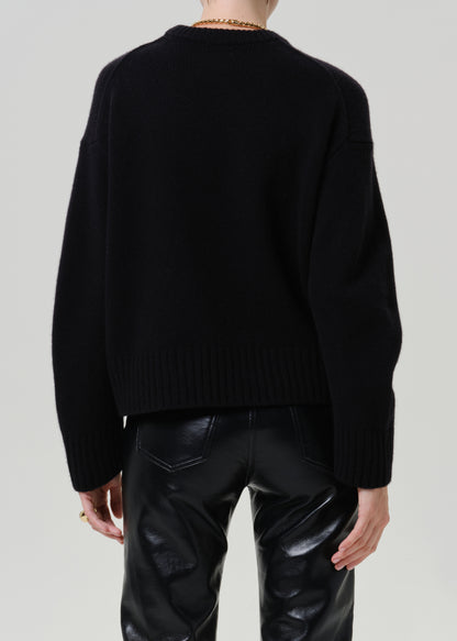 A person shown from the back wearing a black knit sweater and shiny black pants against a light gray studio background.