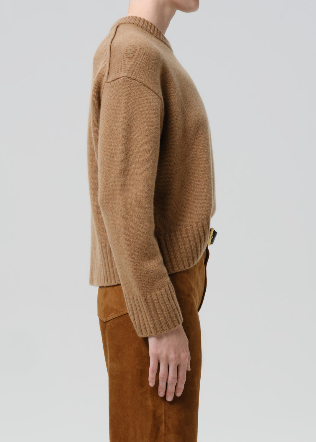 Person wearing a brown sweater and brown pants on a grey background