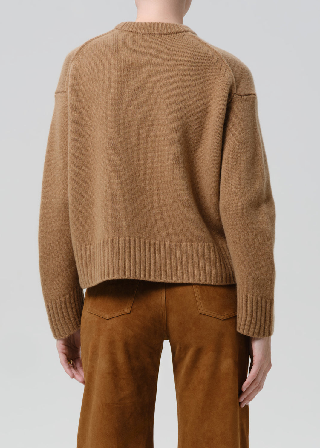 Person wearing a brown sweater and pants on a grey background
