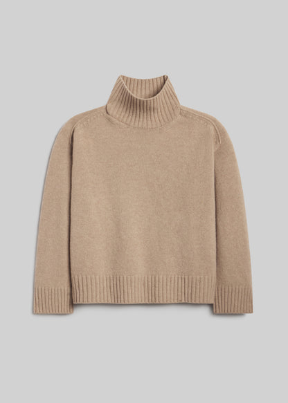 Scout Turtleneck Sweater in Fawn, featuring a relaxed silhouette, light beige knit, ribbed turtleneck, long sleeves, and ribbed cuffs and hem, front view on a grey background.