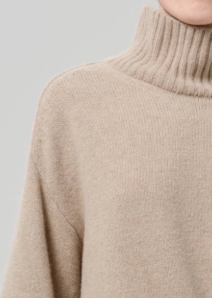Person wearing a beige turtleneck sweater on a grey background