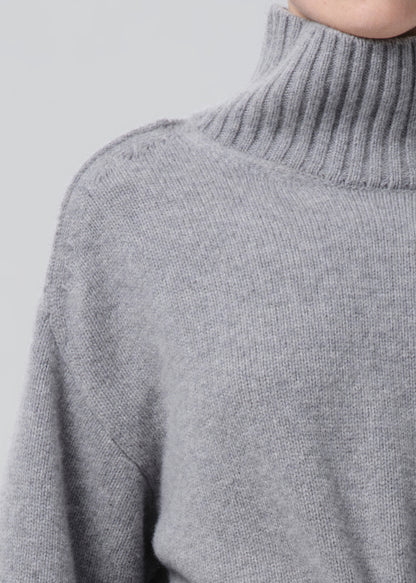Close-up of a light grey oversized turtleneck sweater on a grey background