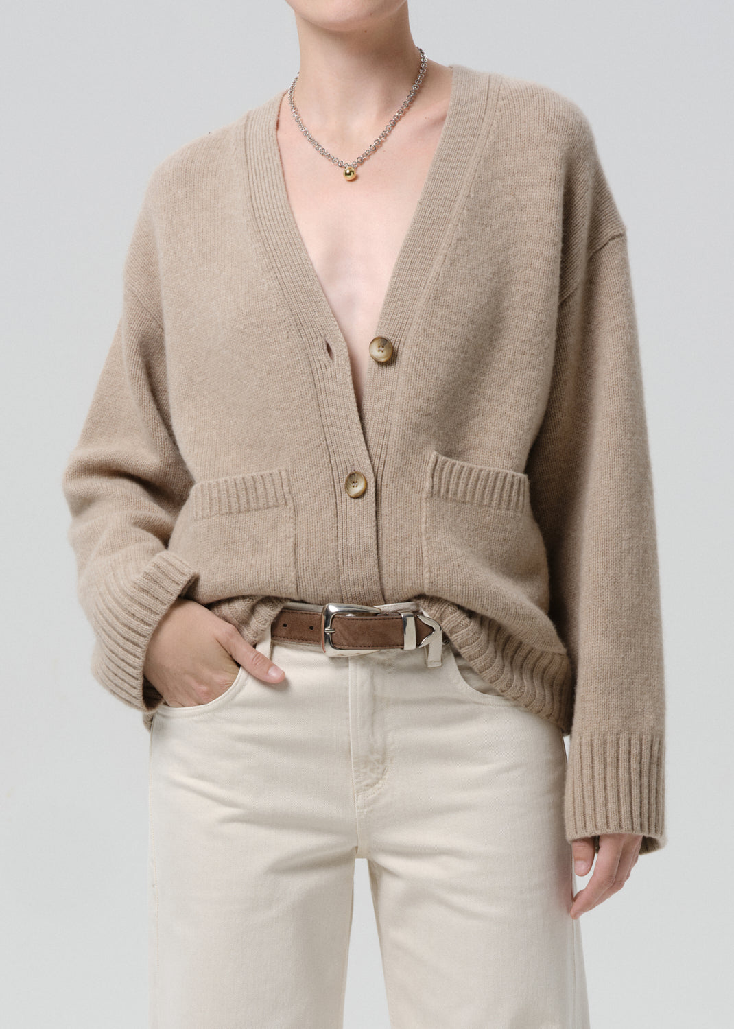 Person wearing a beige cardigan over a grey background