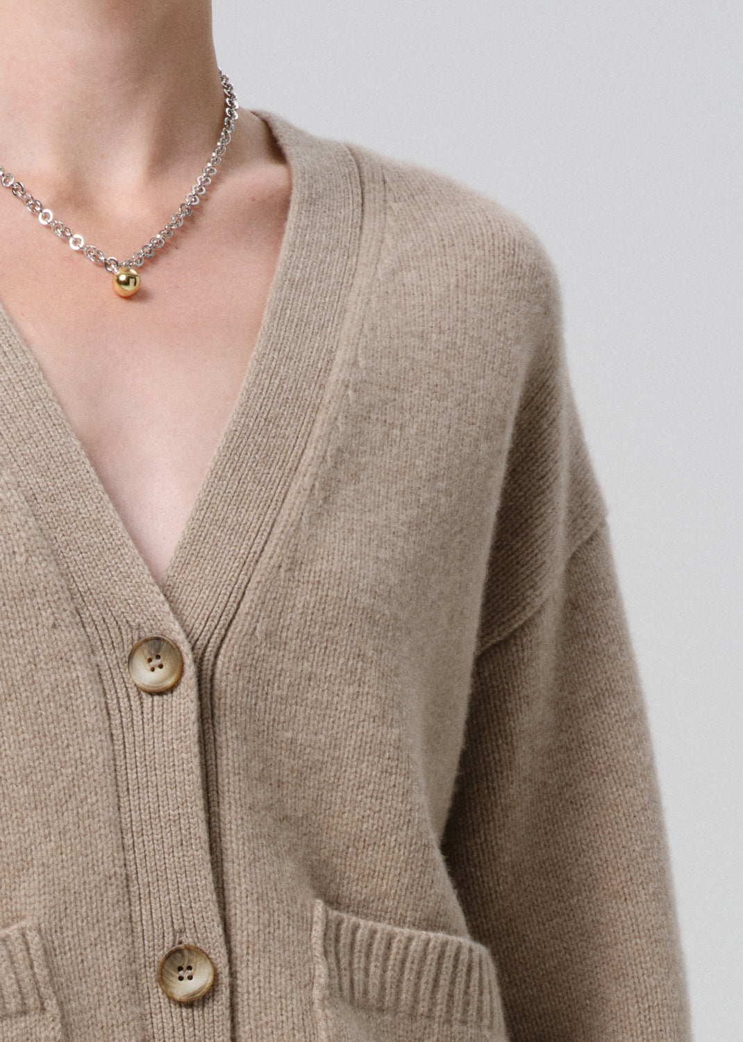 Close-up of a person wearing a beige cardigan with a grey background
