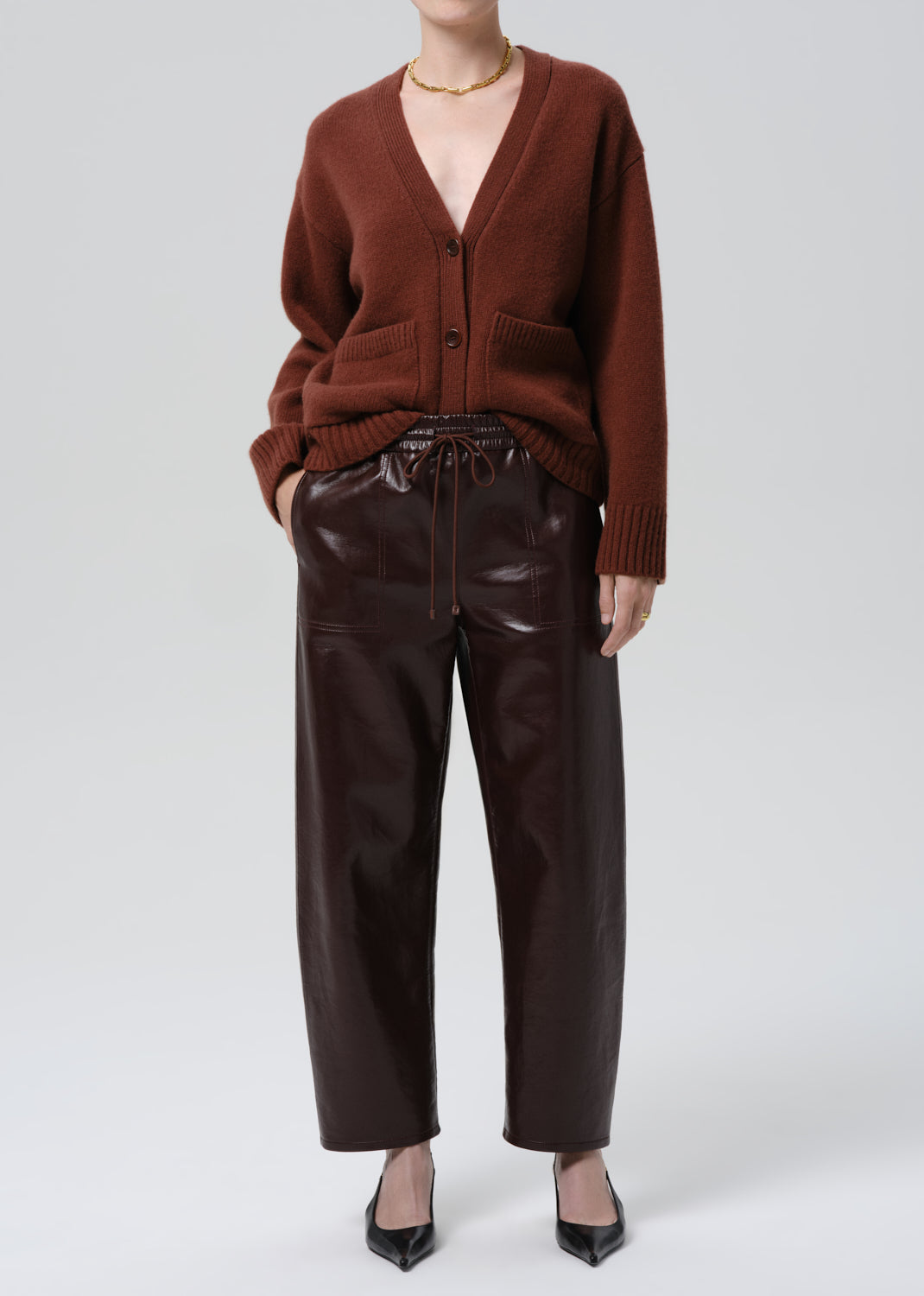Person wearing a brown cardigan and leather pants on a grey background