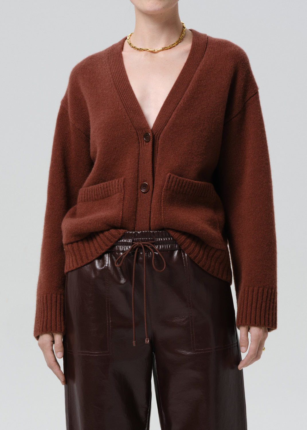 Person wearing a brown cardigan over a black top with leather pants on a grey background