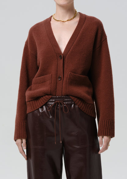 Person wearing a brown cardigan over a black top with leather pants on a grey background