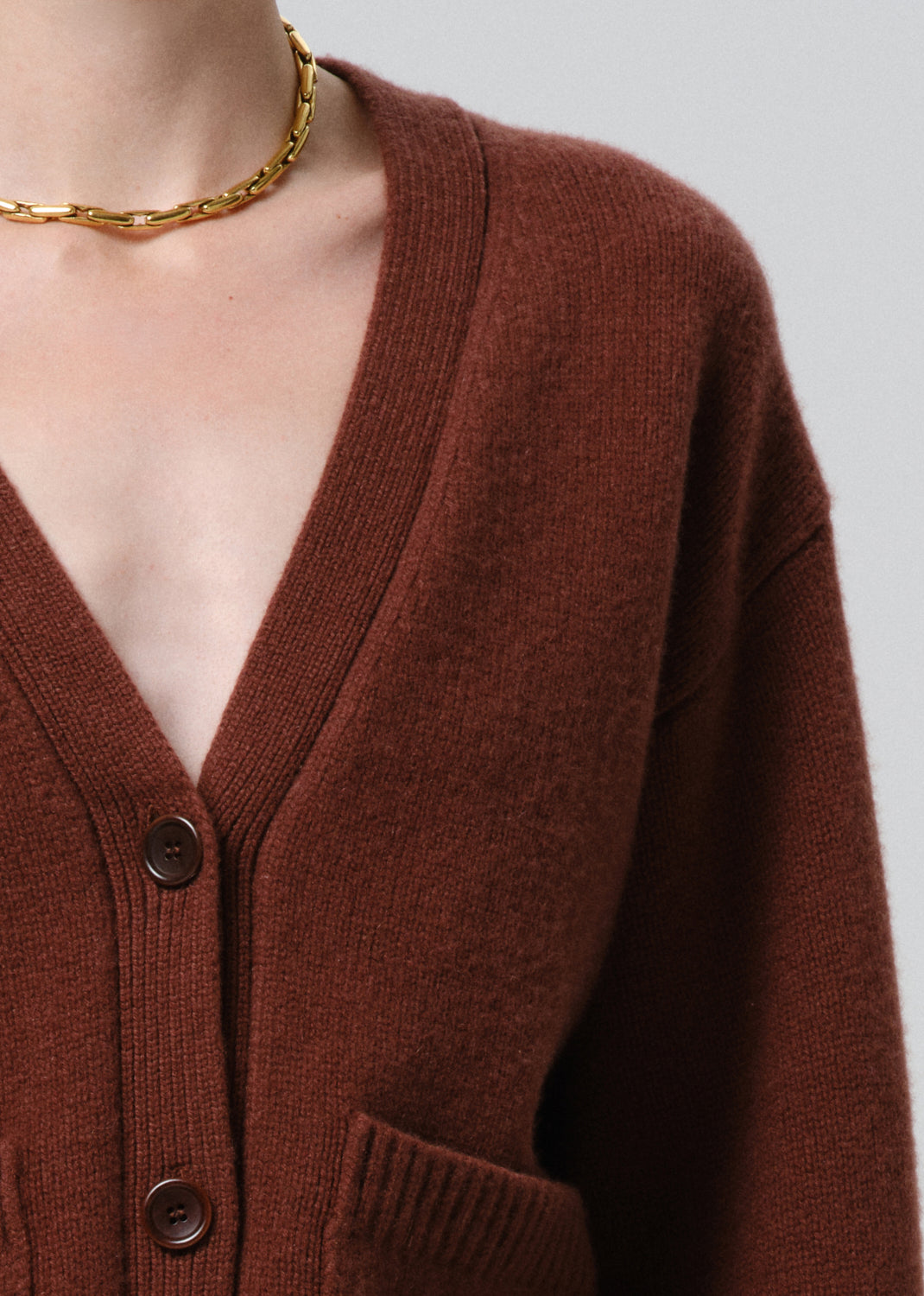 Brown cardigan worn by a person with a gold necklace on a grey background